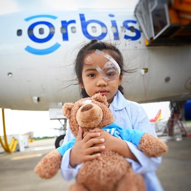 A child who received help from Orbis International standing in front of a plane